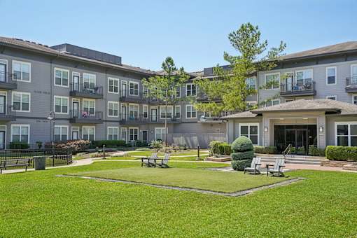 A large grassy area in front of apartment buildings with a tree and benches at Highline Urban Lofts Apartments, Cypress, TX