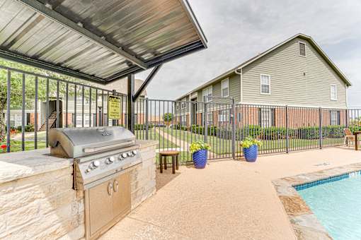 Outdoor grilling area with builtin barbecue and pool at Arbors Of Corsicana Apartments, Corsicana, TX