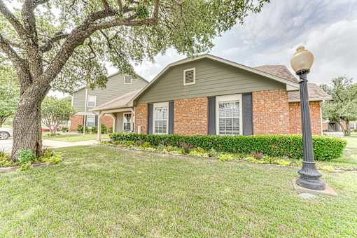 Brick exterior with established trees and landscaping at Arbors Of Corsicana Apartments, Texas