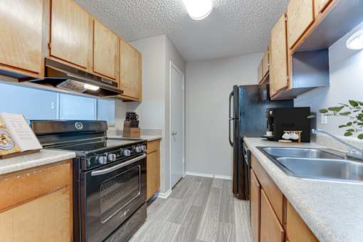 Galley kitchen with black appliances and wood cabinetry at Arbors Of Corsicana Apartments, Corsicana