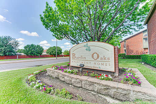 A sign for Bardin Oaks Apartment Homes sits in front of a tree.