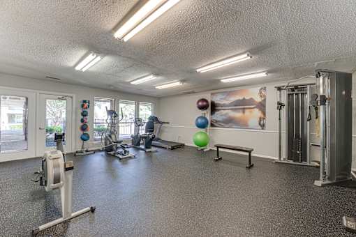 A gym with a variety of equipment including a stationary bike, a treadmill, a rowing machine, a bench, and a wall with a poster.
