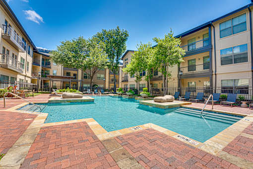 A swimming pool surrounded by brick walkways and residential buildings.