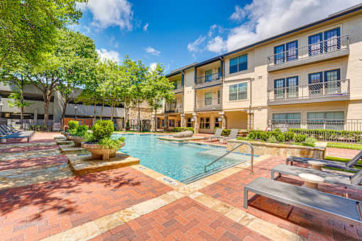 A pool surrounded by a brick patio and a building in the background.