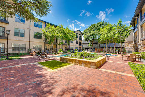 A sunny day at a brick courtyard with a pool and trees.
