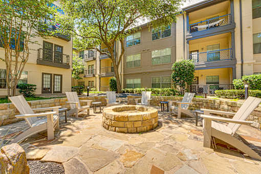 A courtyard with a fire pit surrounded by chairs and trees.