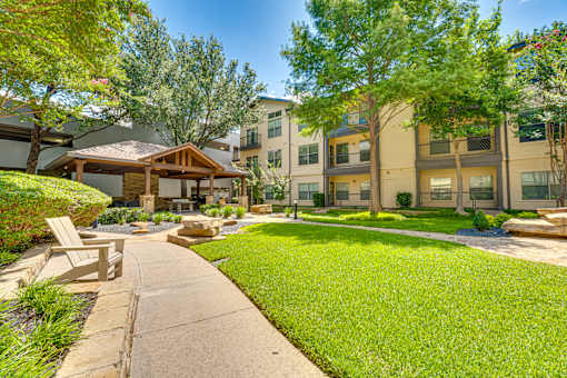 A sunny day at a well-kept apartment complex with a grassy area and a wooden bench.