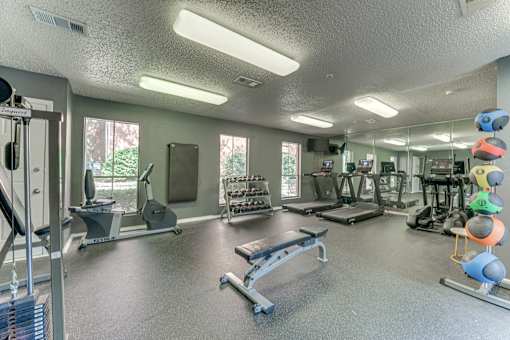 A gym with a variety of equipment including a bench press, a treadmill, and a rowing machine at Copper Hill Apartments, Texas, 76021