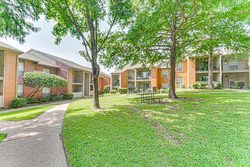 A grassy area with a bench and trees in front of apartment buildings at Copper Hill Apartments, Bedford