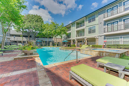A pool surrounded by a patio with sun loungers and trees.