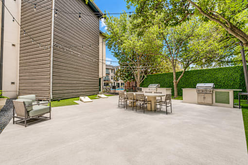 Outdoor grilling area with dining tables and lawn games at The Barton Apartments, Dallas