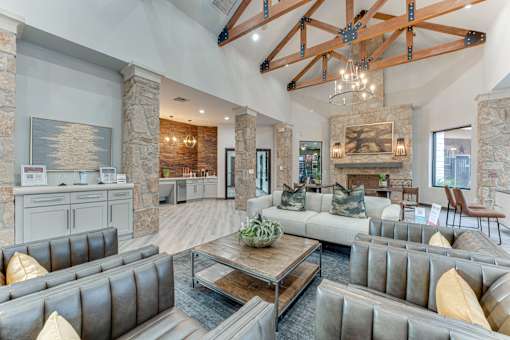 A large, modern living room with a stone fireplace and a high ceiling with exposed beams at Limestone Ranch Apartments, Texas, 75067