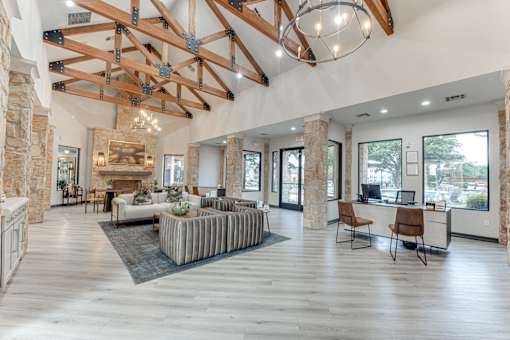 A spacious living room with a stone fireplace and a large wooden beam ceiling at Limestone Ranch Apartments, Texas