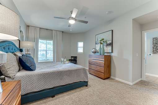A bedroom with a bed, nightstand, and a painting on the wall at Limestone Ranch Apartments, Lewisville, Texas