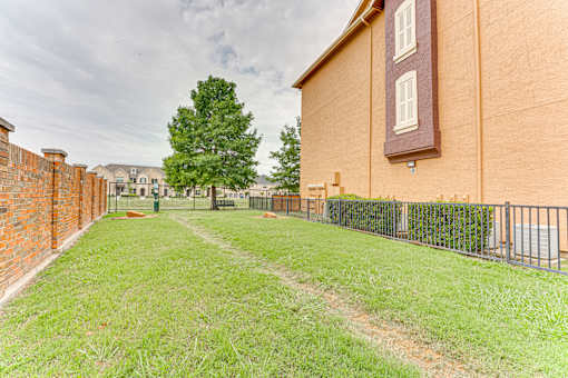 A grassy area in front of a building with a fence and a tree at Limestone Ranch Apartments, Lewisville, Texas
