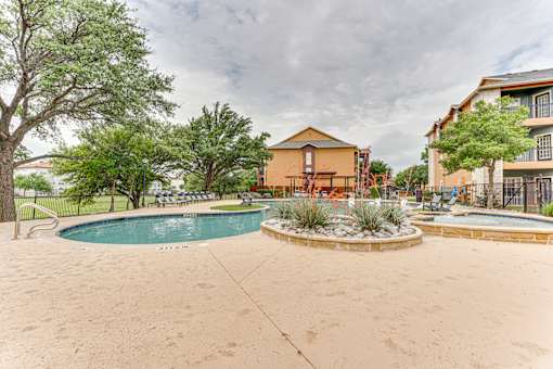 A swimming pool surrounded by a concrete patio and a small garden at Limestone Ranch Apartments, Lewisville 75067