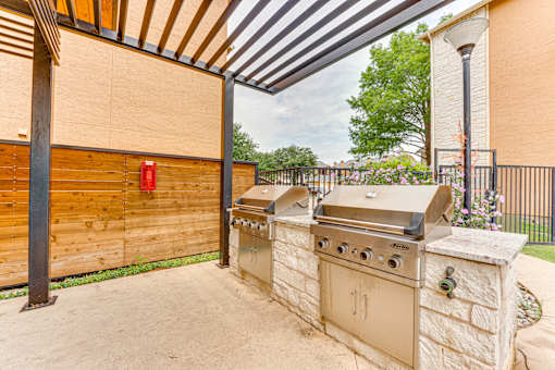 A beige outdoor grill is on a stone pillar under a wooden pergola at Limestone Ranch Apartments, Lewisville