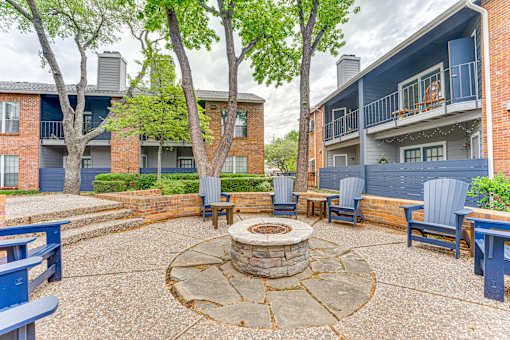 A courtyard with a fire pit surrounded by chairs and trees. at The Manhattan Apartments, Dallas, TX