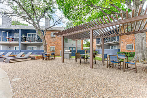 A patio with a pergola and chairs is surrounded by apartment buildings. at The Manhattan Apartments, Dallas, Texas