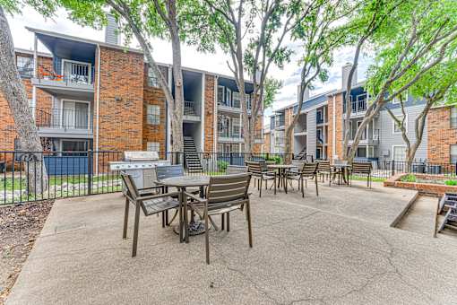 A patio with a table and chairs is surrounded by apartment buildings. at The Manhattan Apartments, Dallas