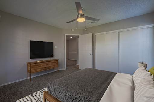 A bedroom with a bed, a television, and a ceiling fan.
