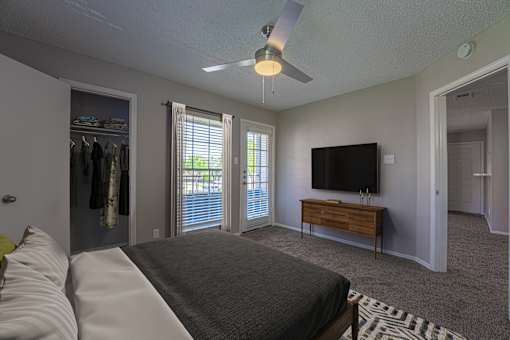 A bedroom with a bed, a dresser, a TV and a ceiling fan.