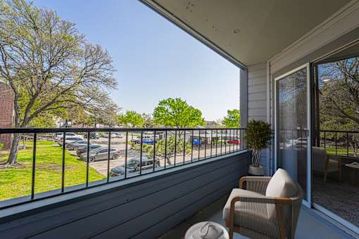 A balcony with a chair and a potted plant overlooking a parking lot.