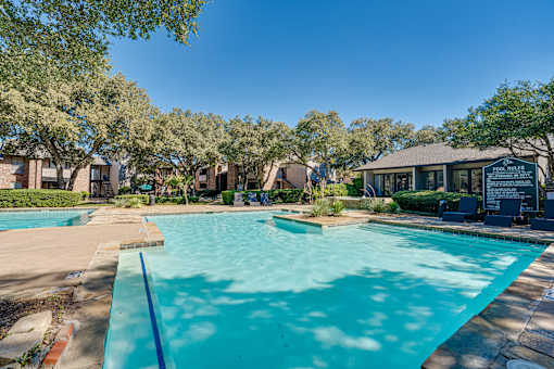 A pool surrounded by trees and a building in the background. at Southern Oaks, Texas