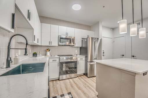 Modern white kitchen with stainless steel appliances and island at The Barton Apartments, Texas