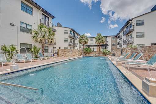 Resort style pool with stone wall and lounge chairs at Vue Live Oak Apartments, Dallas, TX