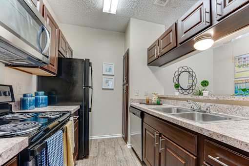 A kitchen with a black refrigerator and brown cabinets. at Wilson Crossing, Cedar Hill