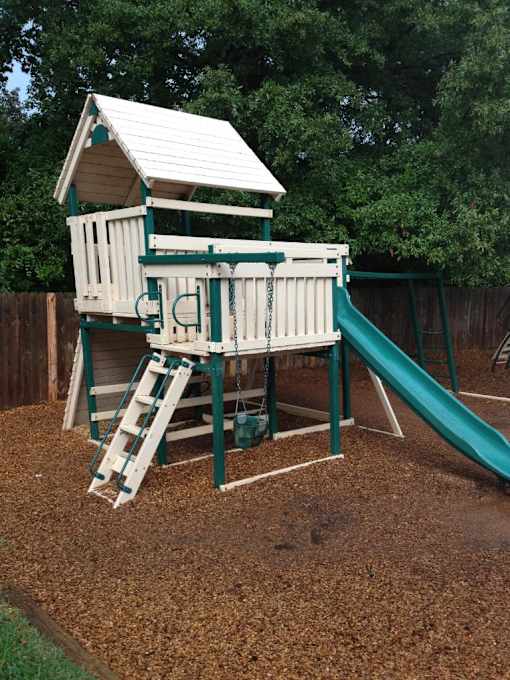 A wooden playset with a green slide in the backyard.