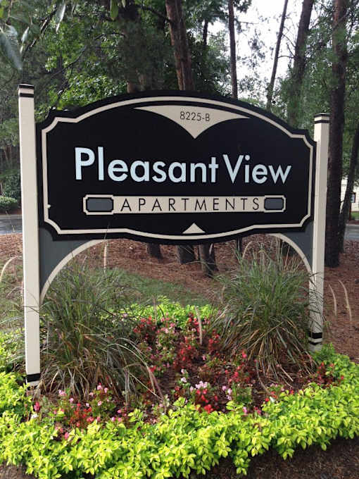 A sign for Pleasant View Apartments is shown in front of a wooded area.