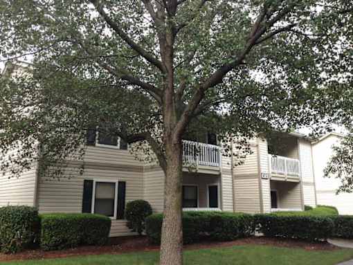 A tree in front of a building with a balcony.