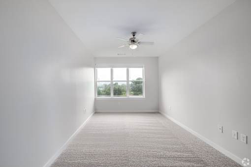 A spacious room with a ceiling fan and a large window.