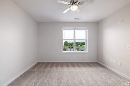 A room with a ceiling fan and a window overlooking a balcony.