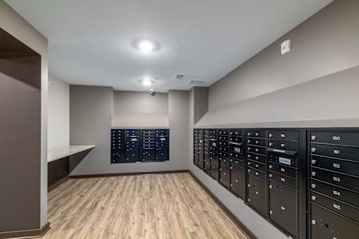 A room with a wooden floor and a wall of black mailboxes.