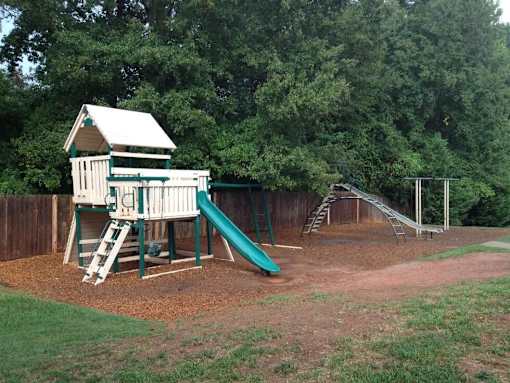 A playground with a green slide and a wooden structure.