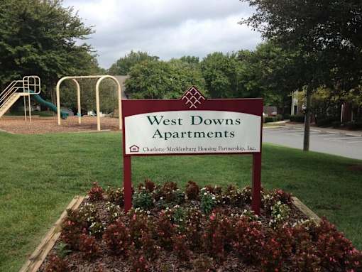 A sign for West Downs Apartments sits in a flower bed.