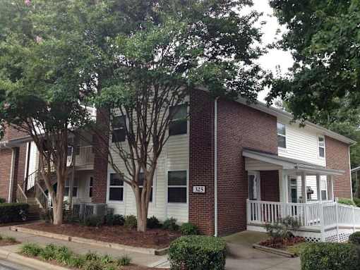 A two-story house with a white front porch and a tree in front.