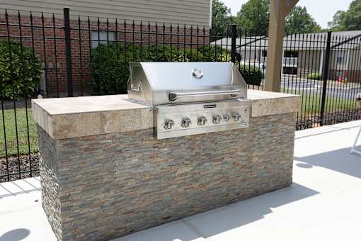 A stone and concrete outdoor grill with a silver lid and four burners.