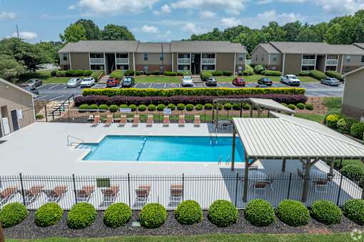 A swimming pool surrounded by a fence and bushes in front of a building.