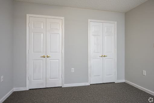Two white doors in a room with carpeted floor.