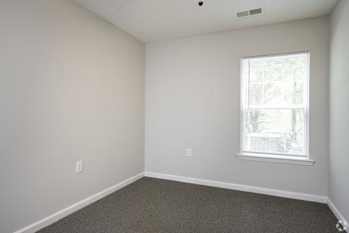 A room with a window and a carpeted floor.