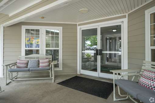 A white bench with red and white pillows sits on a porch.