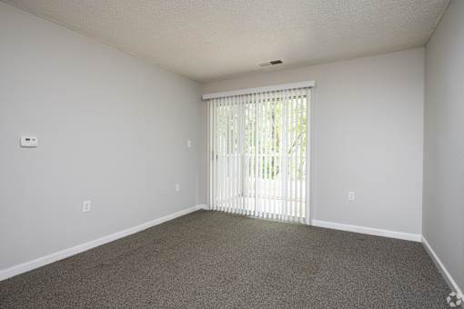 A room with a carpeted floor and a window with blinds.
