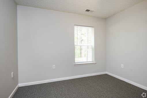 A room with a window and a carpeted floor.