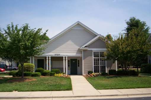 A house with a grey roof and white trim is surrounded by greenery.