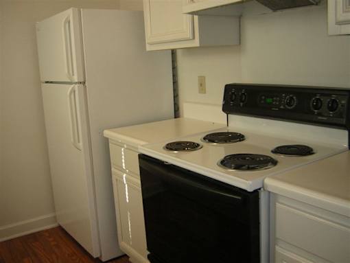 A black stove top oven with four burners and a white refrigerator in a kitchen.