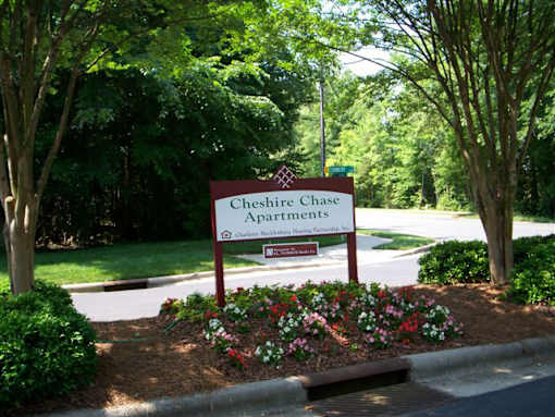 A sign for Cheshire Chase Apartments is surrounded by flowers and trees.